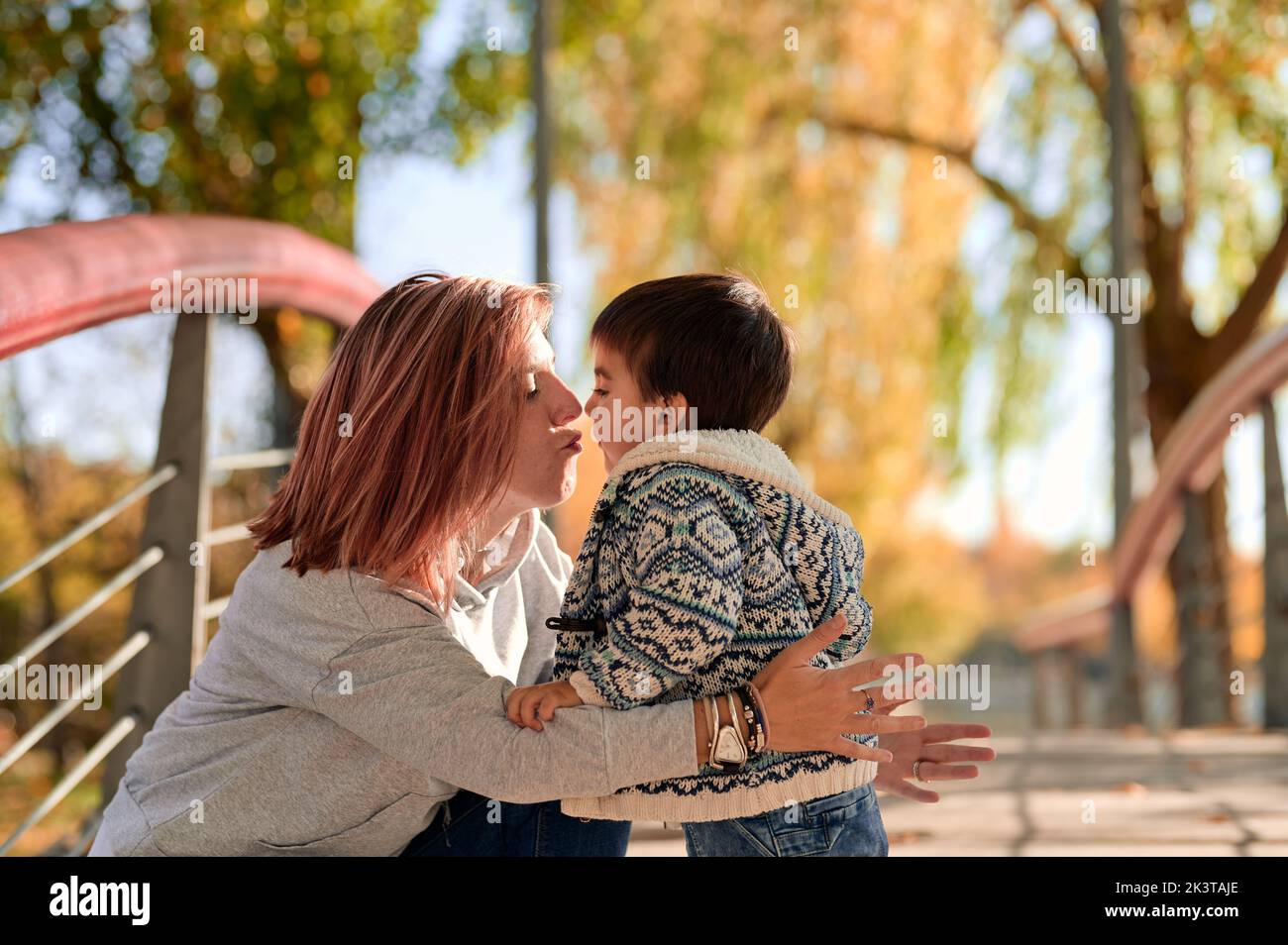 Vista lateral de una madre cariñosa besando a su hijo pequeño mientras pasaban tiempo juntos en el parque en otoño Foto de stock