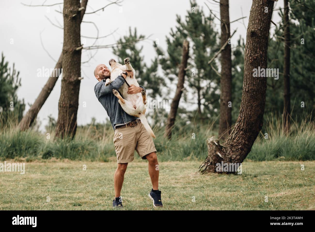 Hombre activo sosteniendo en brazos al adorable Labrador Retriever mientras se ríe al aire libre Foto de stock