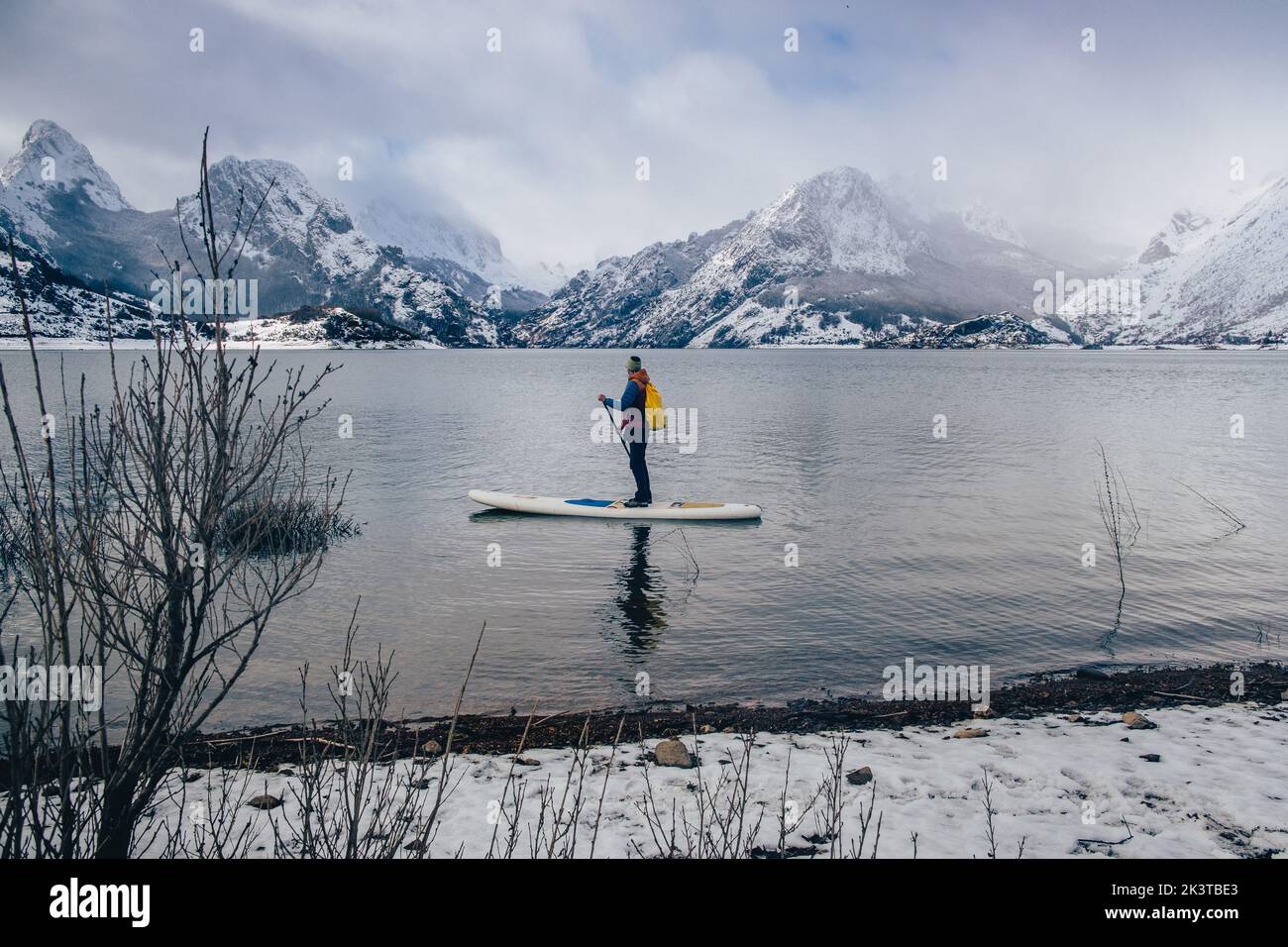 Turista flotando en sup entre la superficie del agua y pintoresca vista de colinas en la nieve Foto de stock
