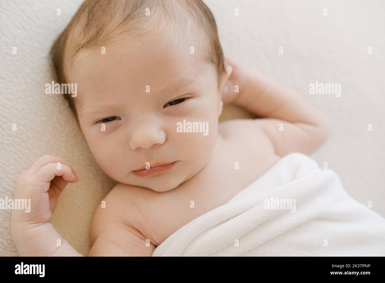 Desde arriba adorable bebé recién nacido envuelto en una suave manta durmiendo sobre fondo blanco Foto de stock