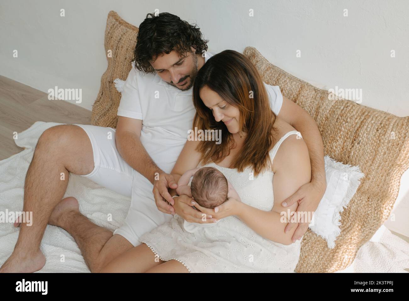 Desde arriba, los padres hispanos abrazan y admiran al bebé mientras se sientan cerca de las almohadas en la habitación en casa Foto de stock