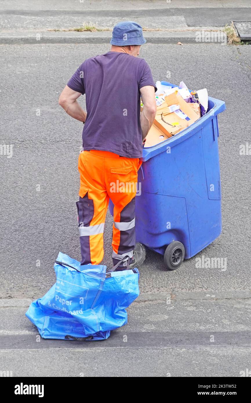 Vista trasera del binman vaciando el contenido del consejo azul emitió la bolsa de reciclaje de cartón de papel doméstico en el cubo de rueda y dejándolo en el pavimento Reino Unido Foto de stock