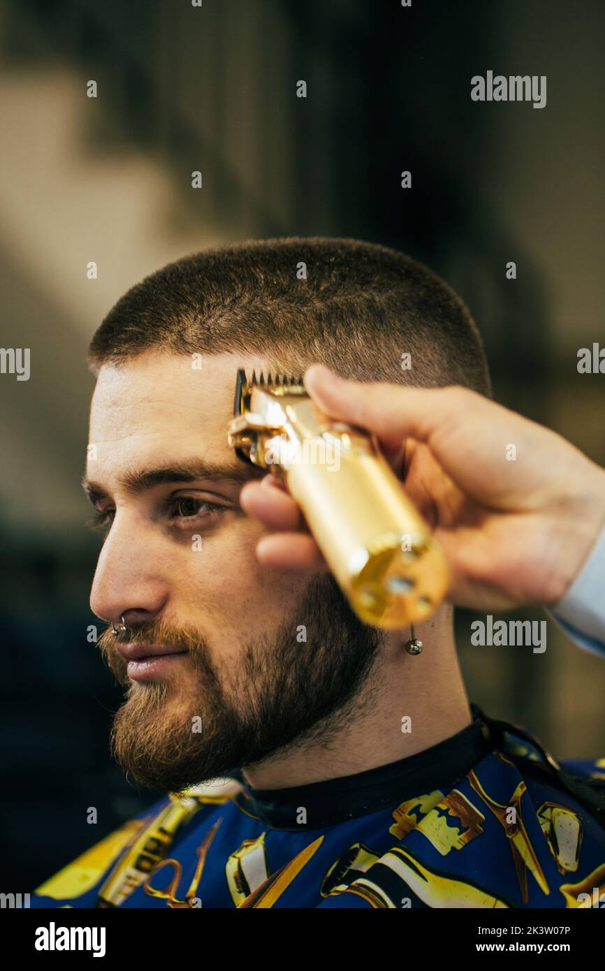 Un pelador corta el pelo de un cliente con un cortapelos Foto de stock