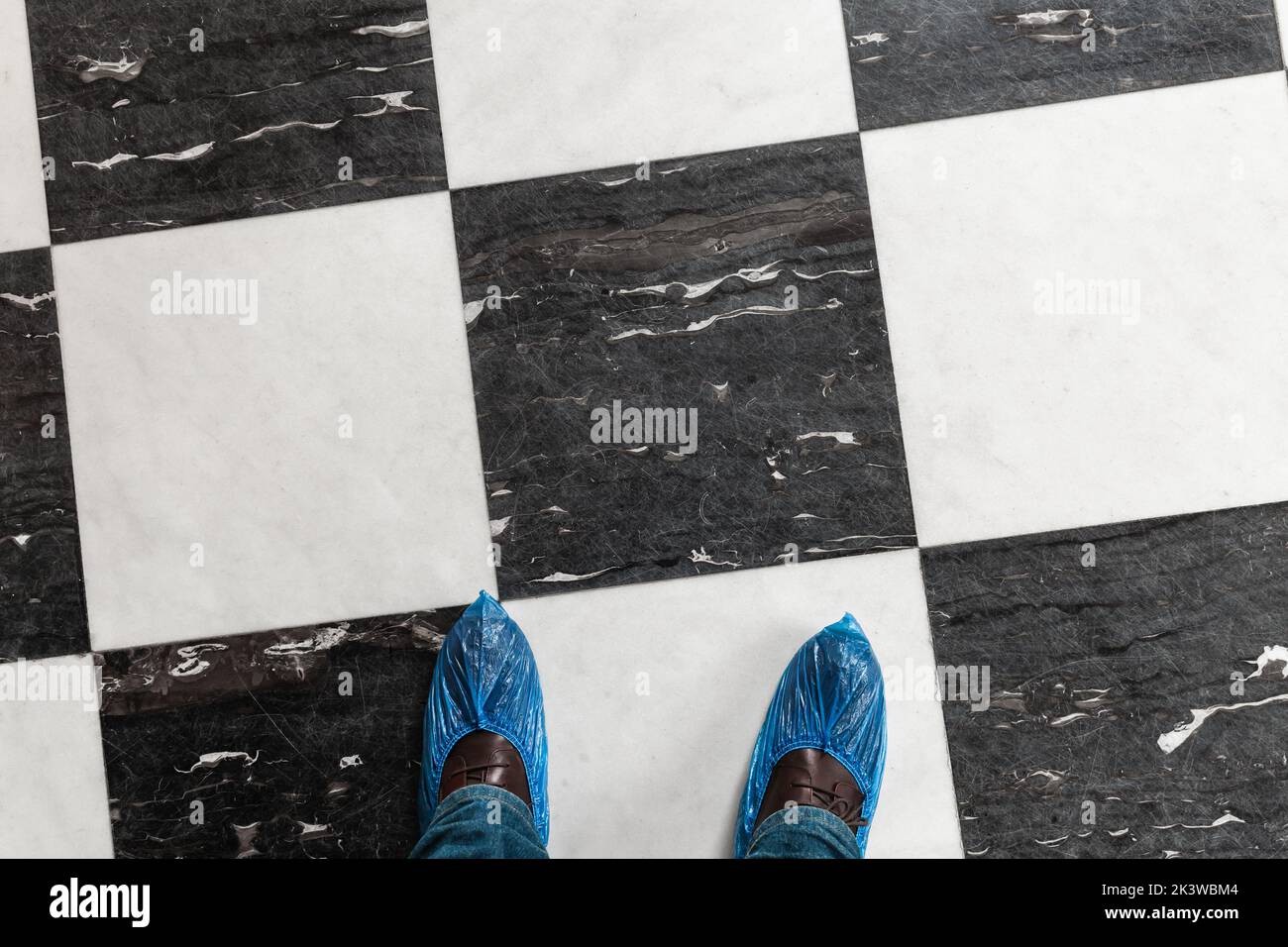 Los pies masculinos en el zapato cubren sobre zapatos clásicos parados en el suelo de piedra con patrón clásico del comprobador, vista superior Foto de stock