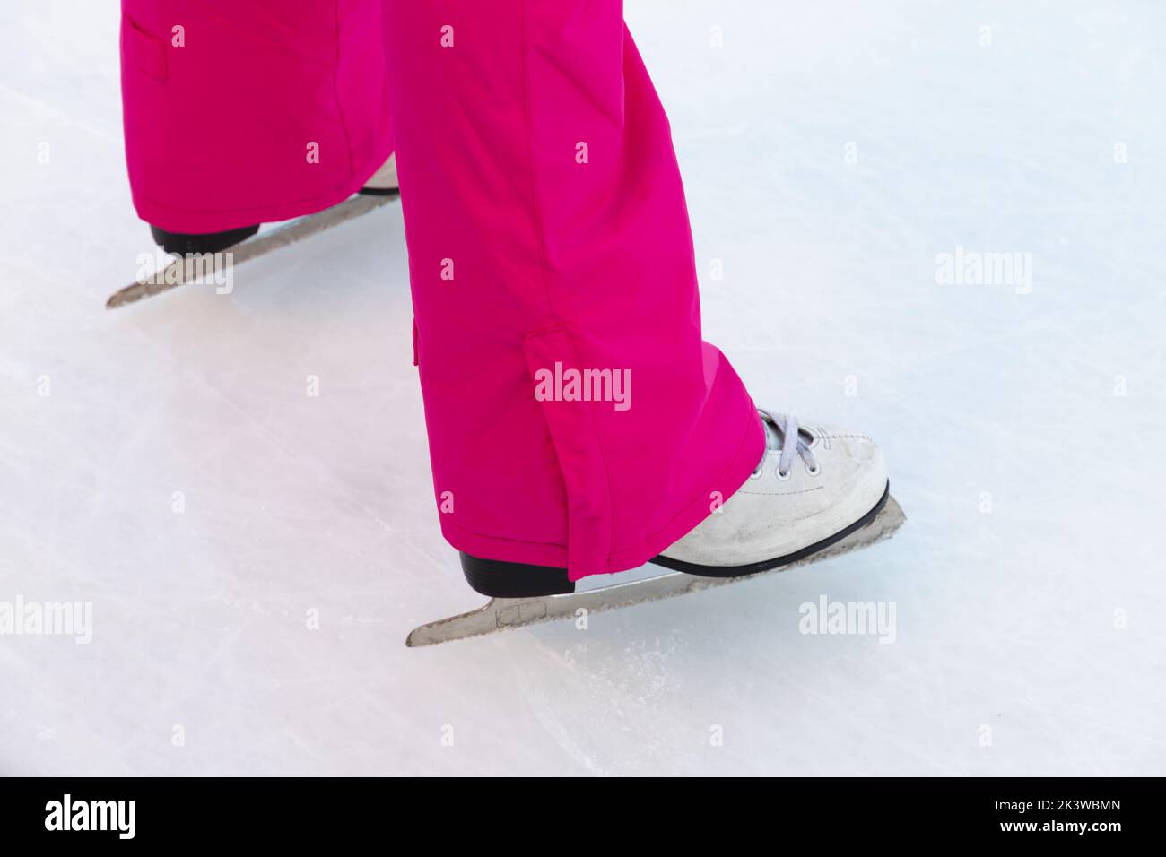 Patas de una chica de color rosa sobre patines en una pista de hielo blanca Foto de stock