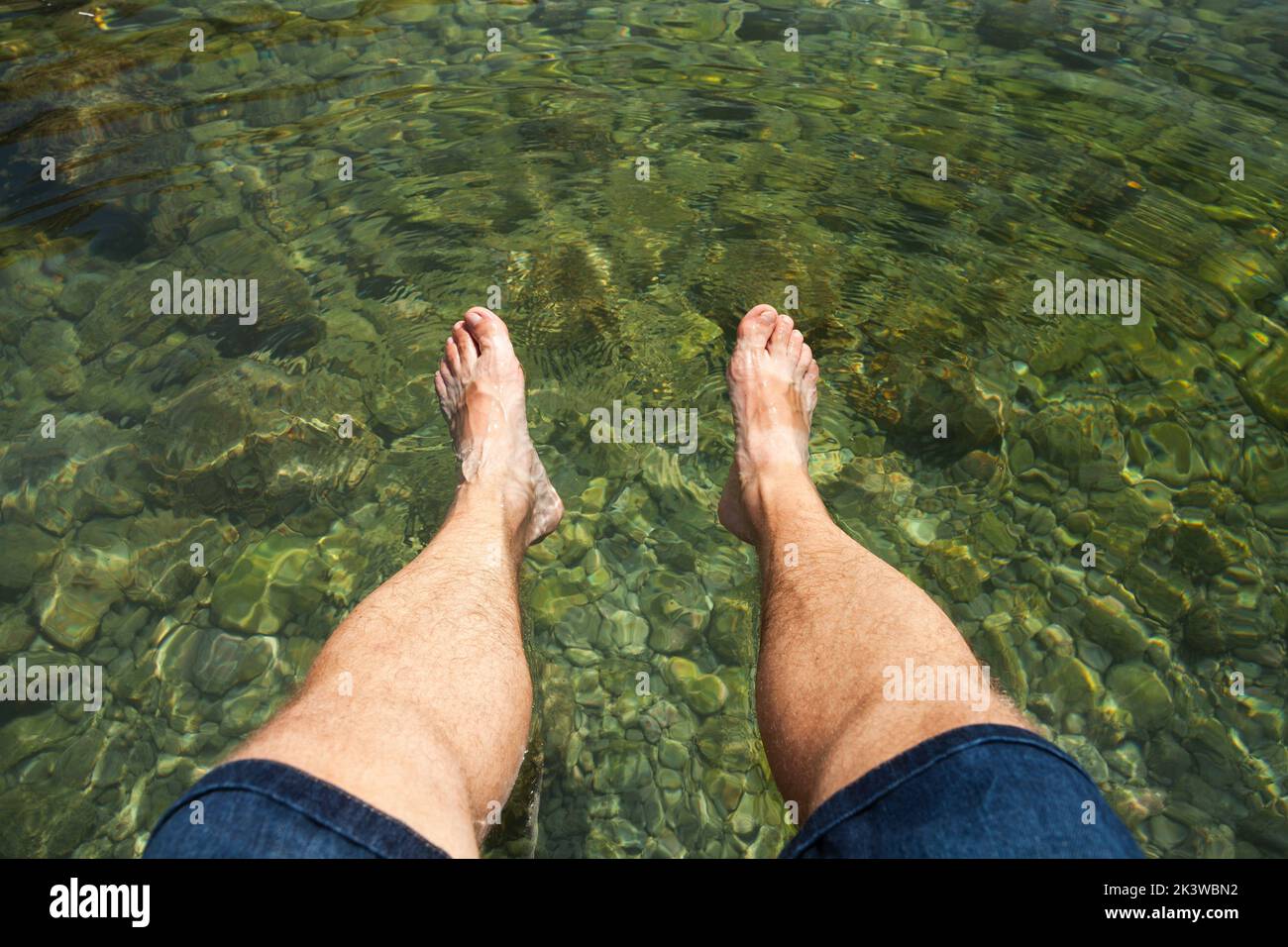 Hombre pies descalzos enfriándose en el agua del mar, vista en primera persona de ángulo amplio Foto de stock