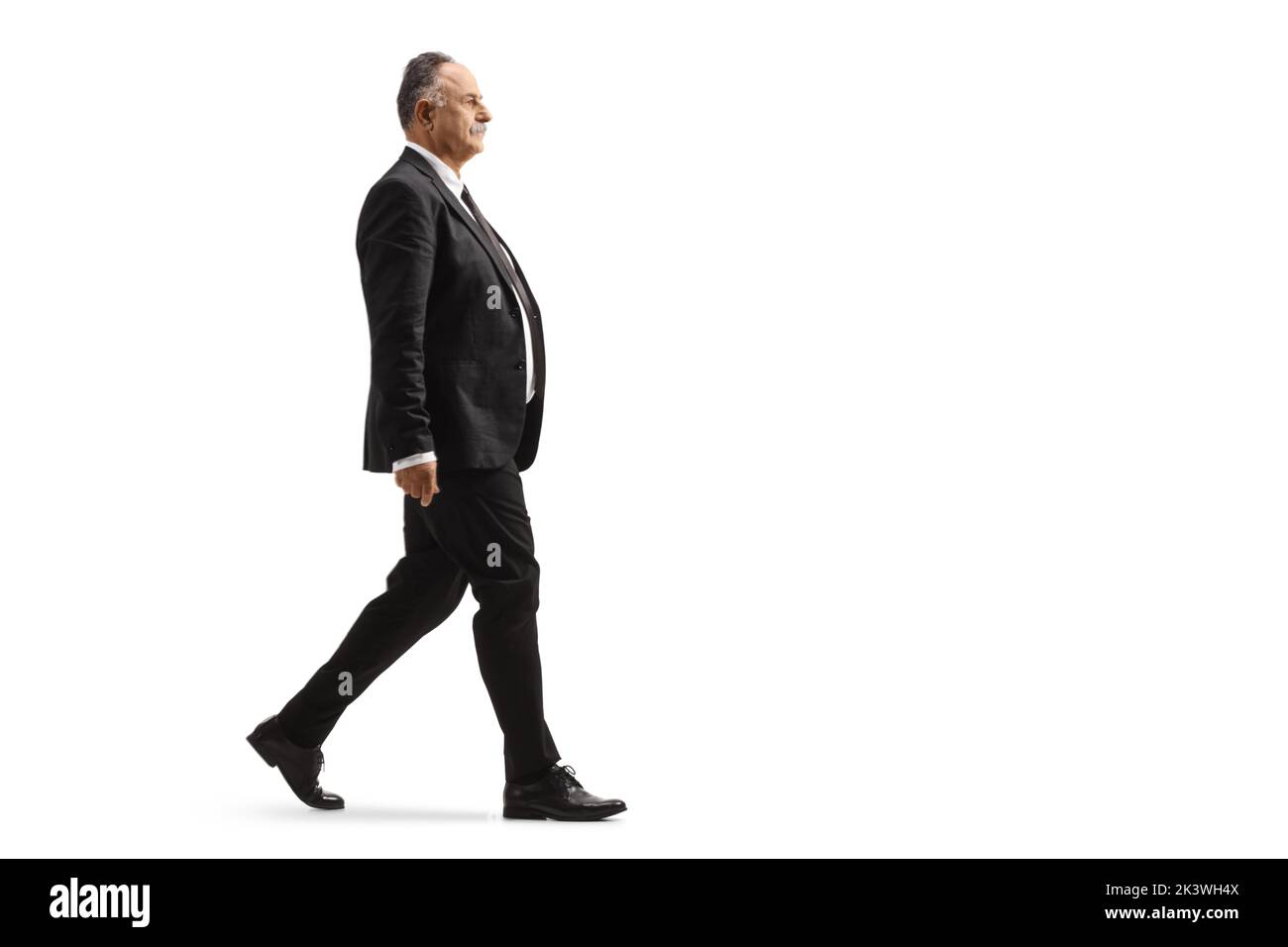 Foto de perfil completo de un hombre de negocios maduro con un traje negro que caminaba aislado sobre fondo blanco Foto de stock