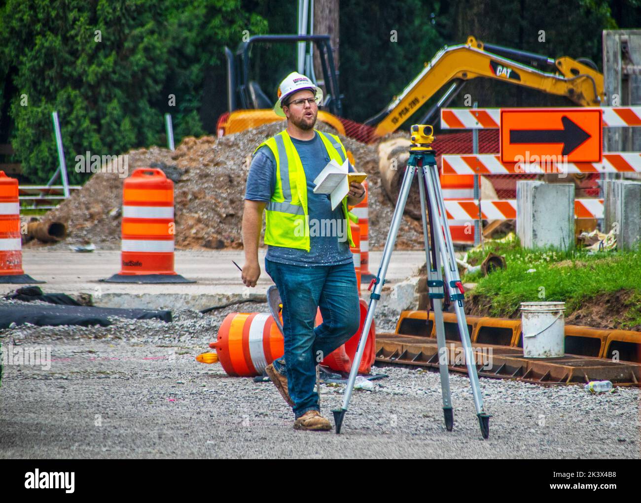 2022 05 13 Tulsa, OK EE.UU. - Surveyer llamando a alguien en el sitio de la construcción con el libro en su mano por trípode con la leva óptica Foto de stock