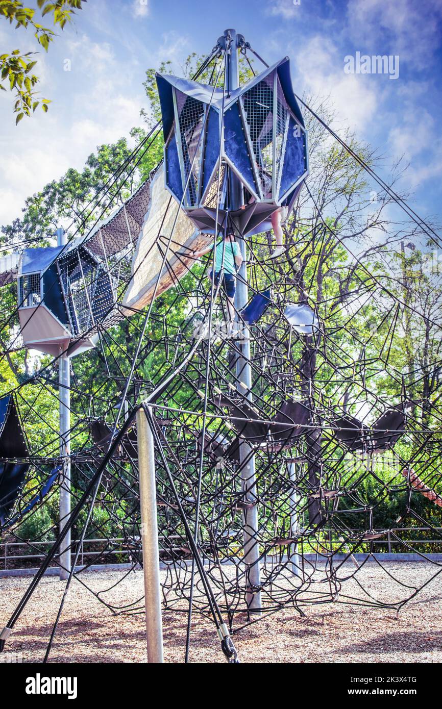 Adolescentes trepando en elaborados equipos de cuerdas en un parque público con árboles en el fondo Foto de stock