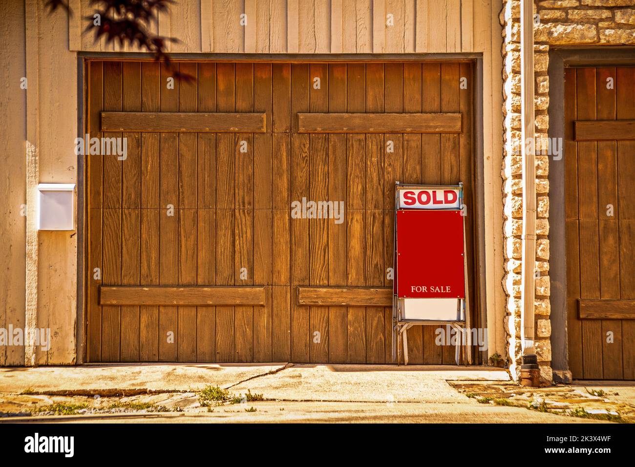 Garaje para dos coches con puertas rústicas de madera con signo de venta diciendo vendido apoyado contra él - Copy Space Foto de stock