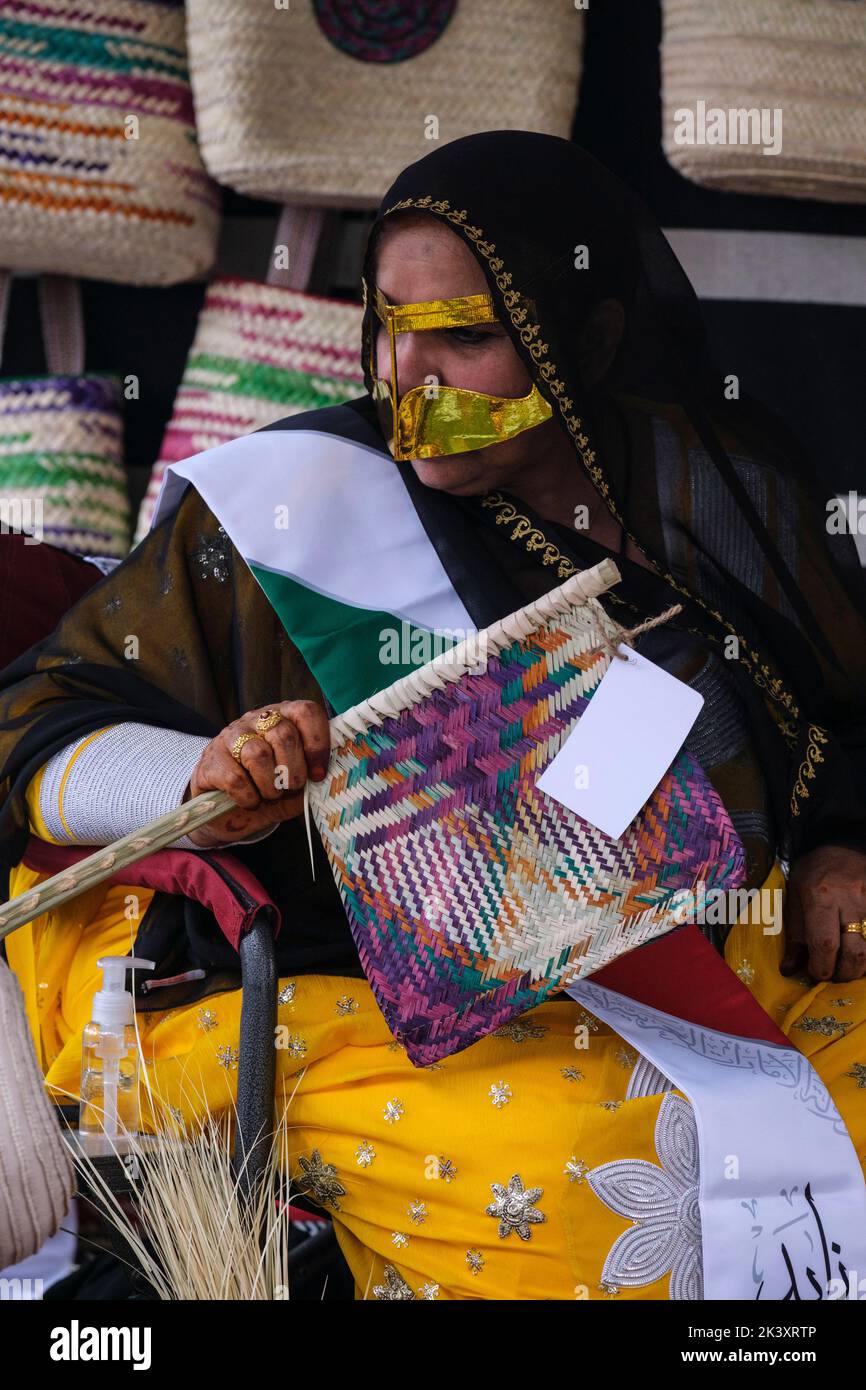 Mujer árabe enmascarada de Abu Dhabi con Abaya en el Festival Folklife demostrando habilidades artesanales tradicionales, sosteniendo un ventilador hecho de fibra de palma datilera. Foto de stock