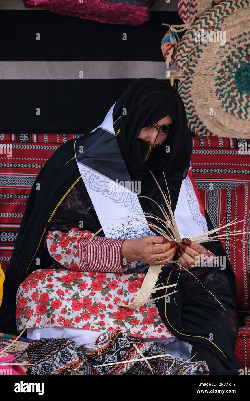 Mujer árabe enmascarada de Abu Dhabi usando un Abaya que hace las bandas de la fibra de la palma de la fecha para el uso en hacer cestas tradicionales de la paja. Foto de stock