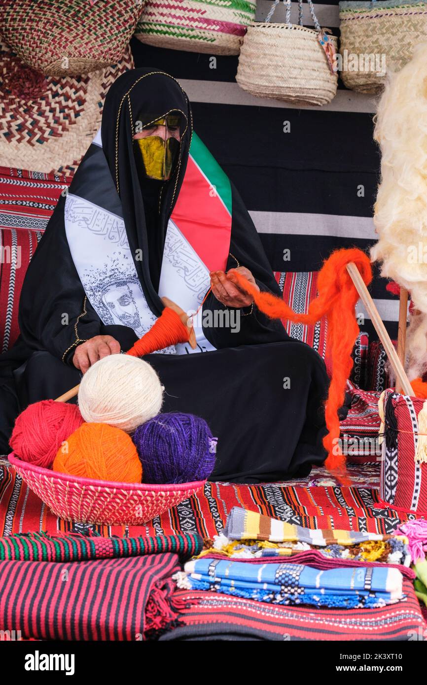 Mujer árabe enmascarada de Abu Dhabi con un Abaya en un Festival Folklife que demuestra las habilidades artesanales tradicionales, poniendo lana en un eje. Foto de stock