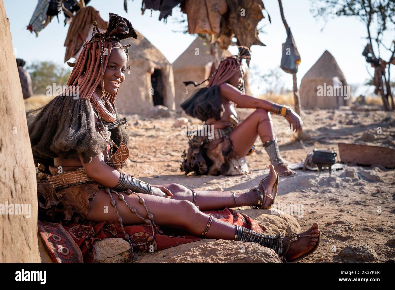 Mujeres himba sentadas fuera de sus chozas en una aldea tradicional de Himba en Namibia, África. Foto de stock