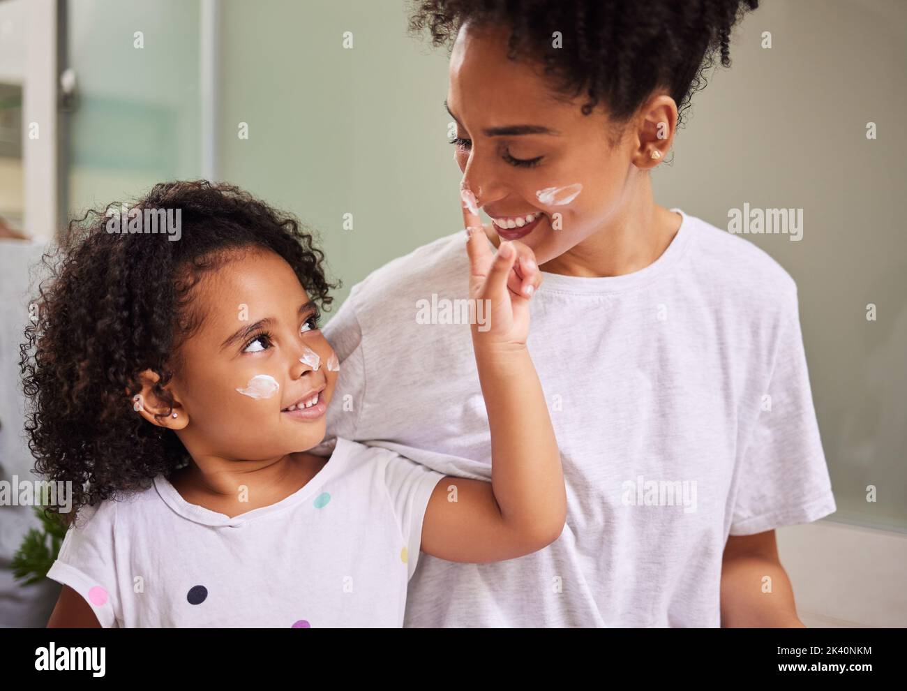 Feliz familia, madre y niña con crema de cuidado de la piel en la cara por la mañana para vincular en México hogar. Mamá latina sonriente con un niño pequeño y alegre Foto de stock