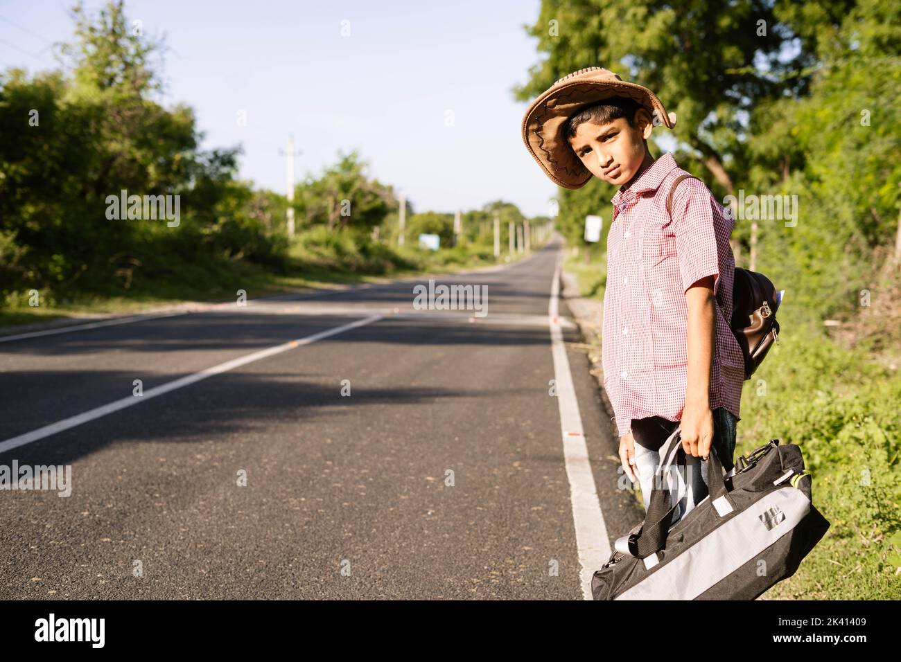 Niño adolescente indio esperando un autobús o un taxi en la carretera durante su viaje de vacaciones - concepto de viaje, vacaciones de fin de semana y vida de ocio. Foto de stock