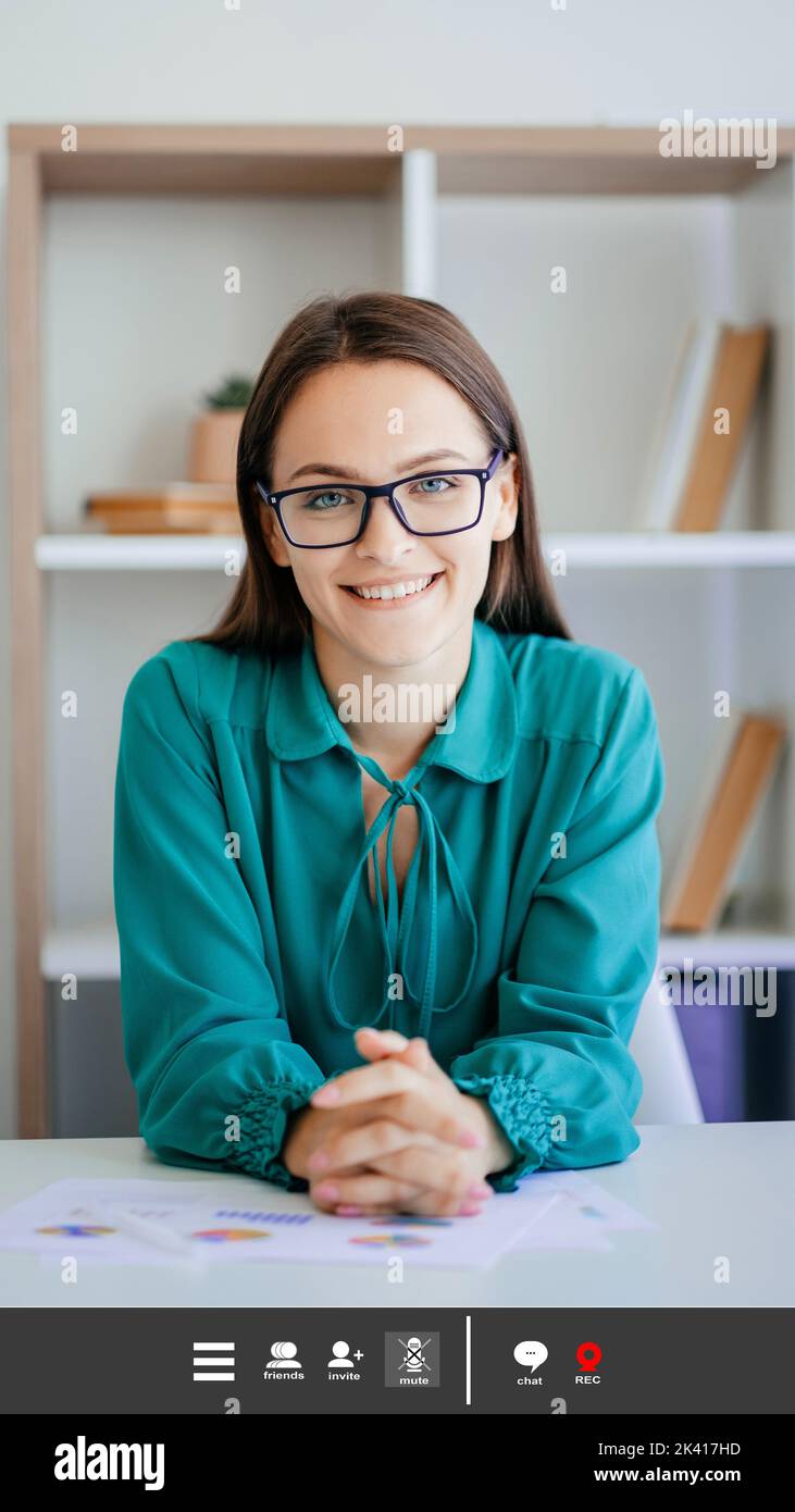Consulta en línea. Mujer positiva. Maqueta de pantalla. Sonriente bonita dama sentado escritorio de trabajo en seminario web en un interior luminoso. Foto de stock