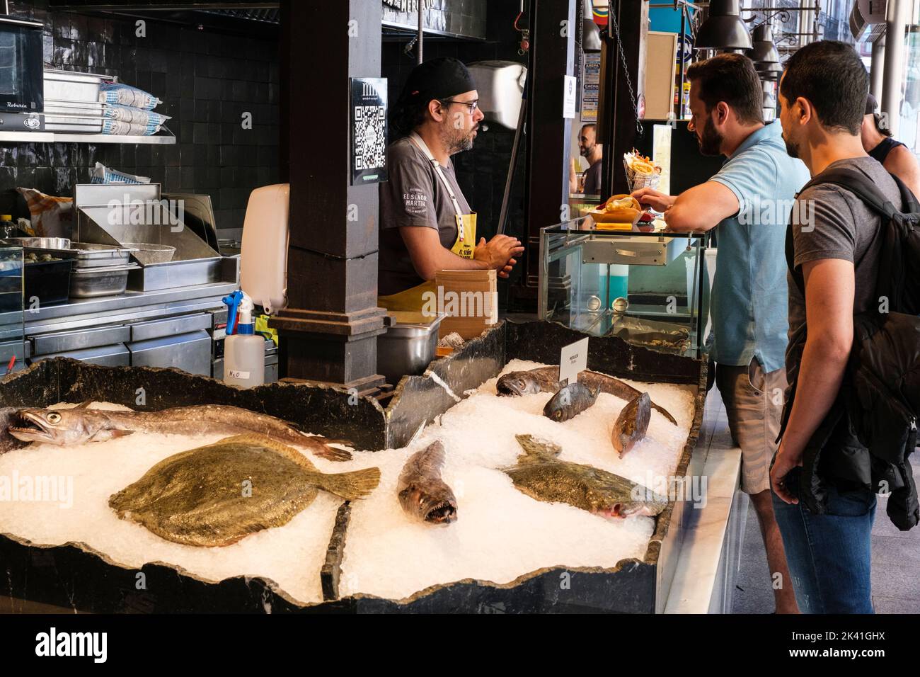 España, Madrid. Mercado de San Miguel. Cliente que compra un Taco de Pescado y Anillos de Cebolla. Foto de stock