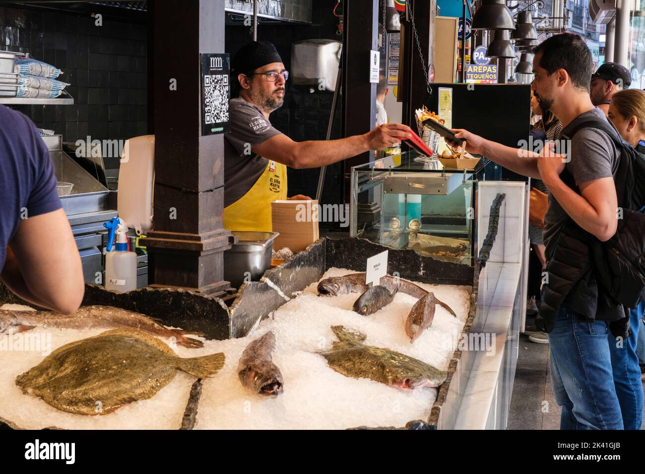 España, Madrid. Mercado de San Miguel. Cliente que utiliza el teléfono para pagar por un Fish Taco. Foto de stock