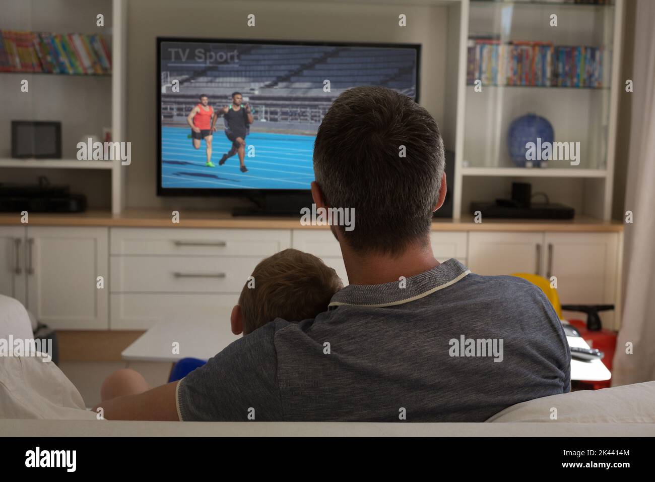 Vista trasera de padre e hijo sentados en casa juntos viendo un evento atlético en la televisión. Deportes, competición, entretenimiento y tecnología concepto digital Foto de stock