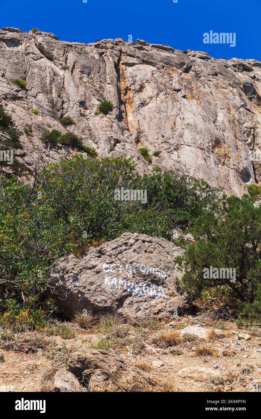 Verano Paisaje de Crimea con texto ruso en una piedra: Ten cuidado, caída de rocas. Las montañas rocosas están en el fondo Foto de stock