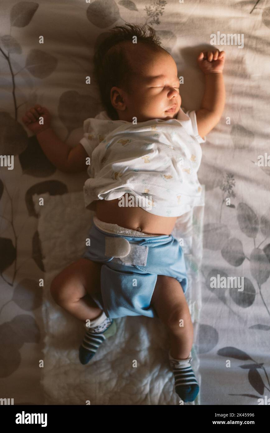 bebé recién nacido usando pañal de tela durmiendo tranquilamente en la cama por la mañana con luz natural y pijama blanco Foto de stock