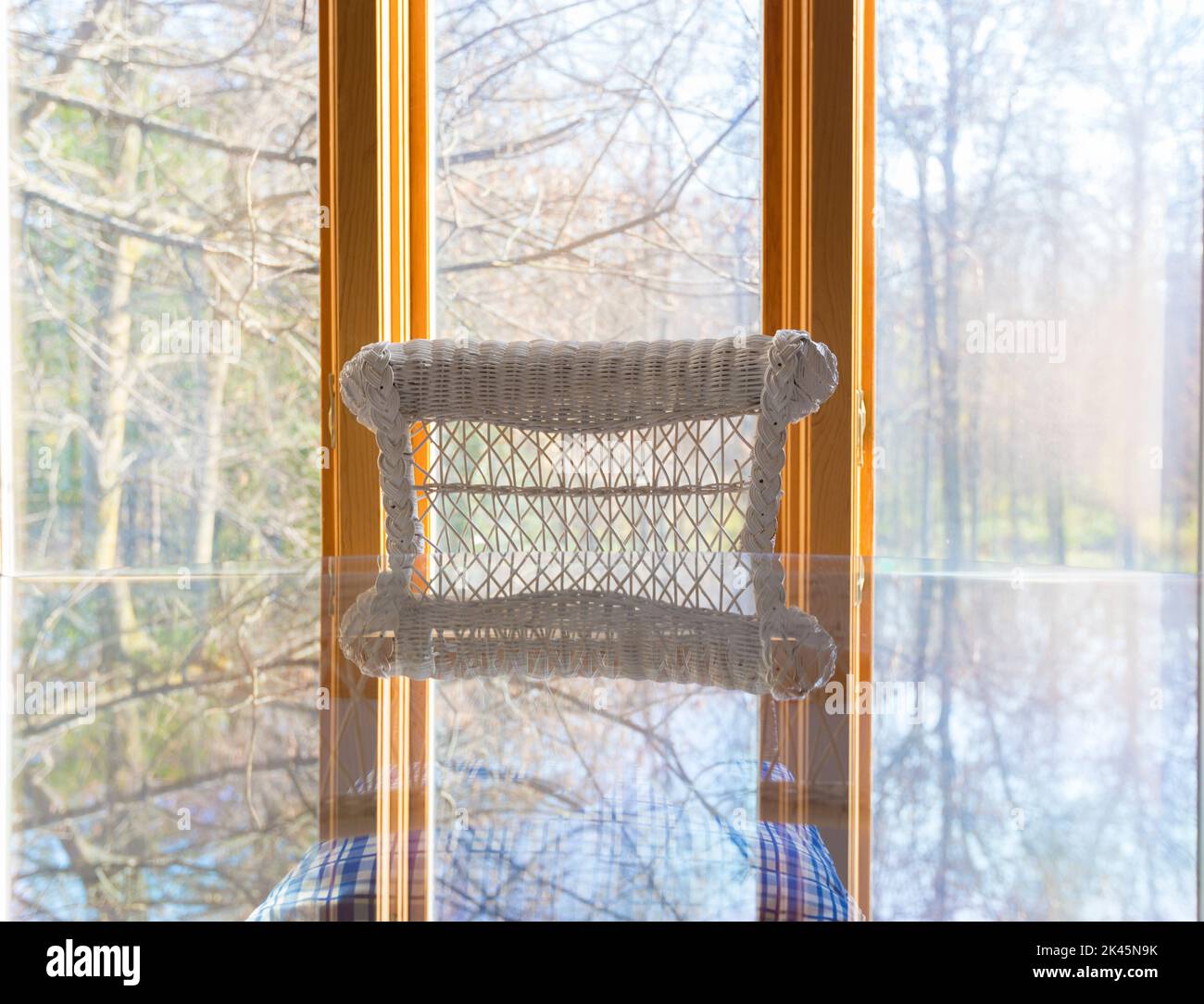 Una ventana panorámica con vistas al bosque, una mesa de vidrio y una silla de caña blanca. Foto de stock