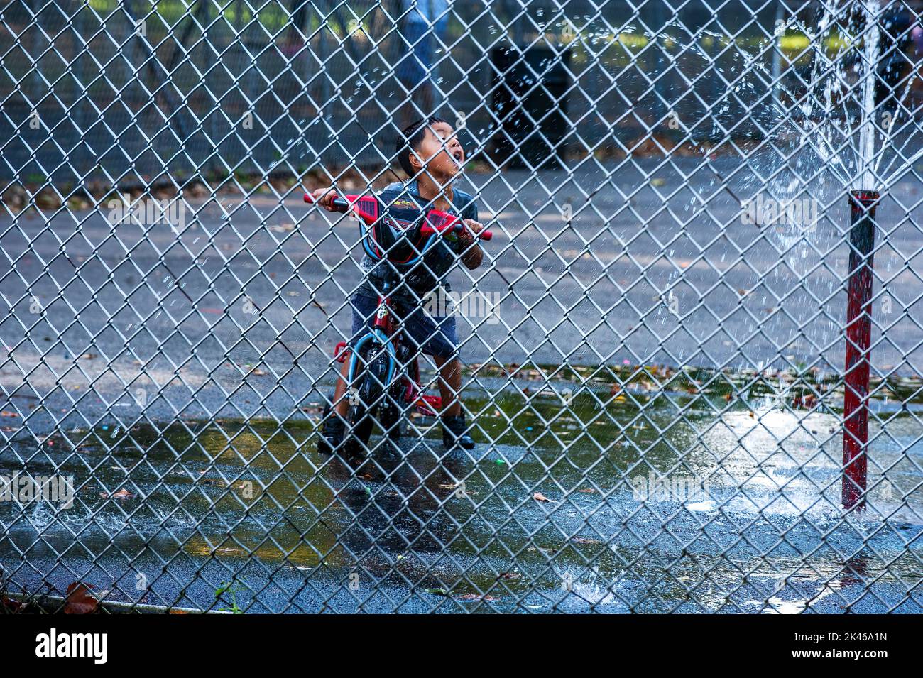 Joven asiático en bicicleta bebiendo de una fuente de agua en Kissing Park en Queens, Nueva York Foto de stock
