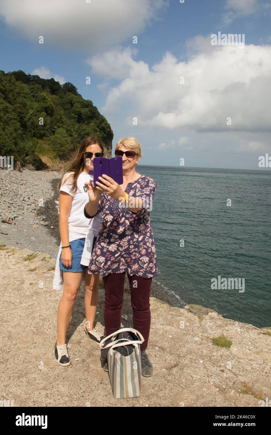 Madre e hija de mediana edad se reunieron y tomando foto selfie en una tableta en la pared de Clovelly Harbour, Devon, Reino Unido Foto de stock