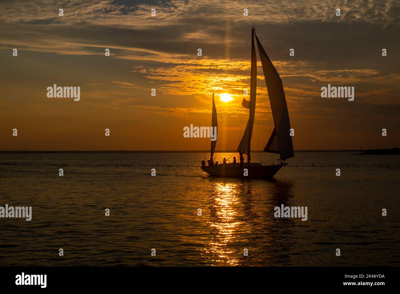 silueta de barco de vela con el sol de la puesta de sol brillante detrás de ella. Foto de stock
