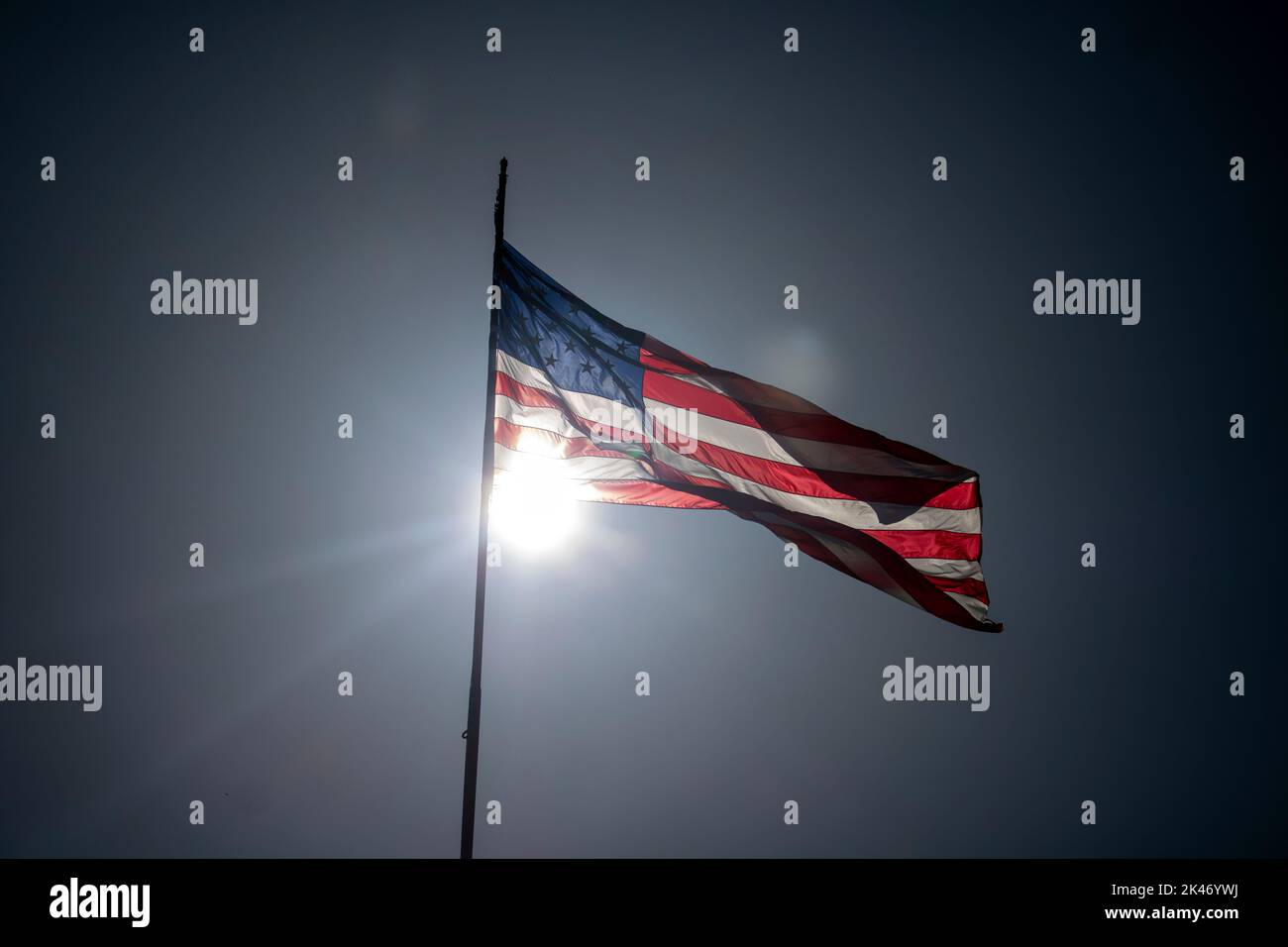 Sol retroiluminado estrellas americanas y bandera de rayas soplando en el viento en un día brillante Foto de stock