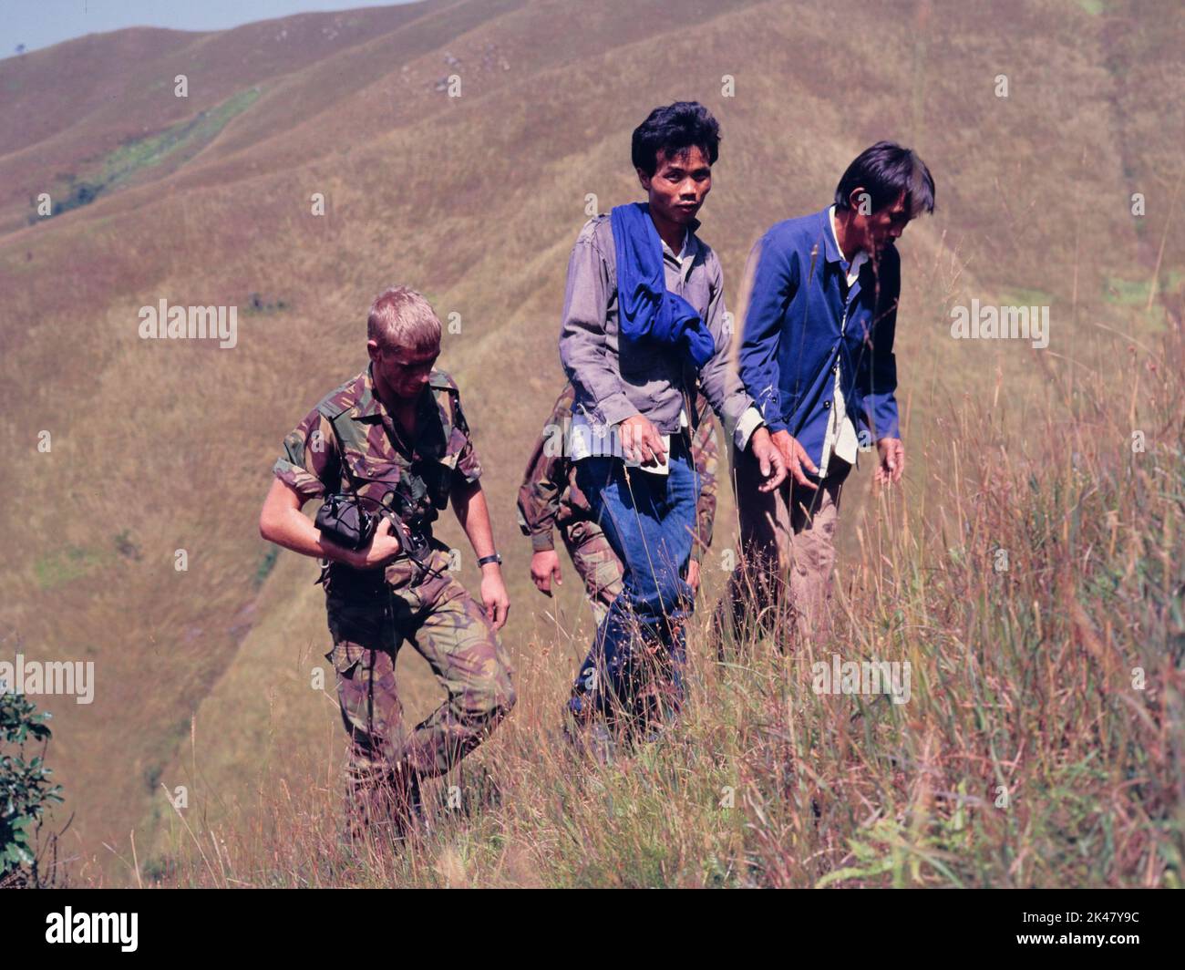 Dos hombres inmigrantes ilegales, que acaban de ser arrestados en Hong Kong, son escoltados hasta una colina cerca de la frontera en los Nuevos Territorios de Hong Kong, por dos soldados del Regimiento de Cheshire, del Ejército Británico. Oct 1984. El soldado de la izquierda lleva un antiguo paquete de radio. Foto de stock