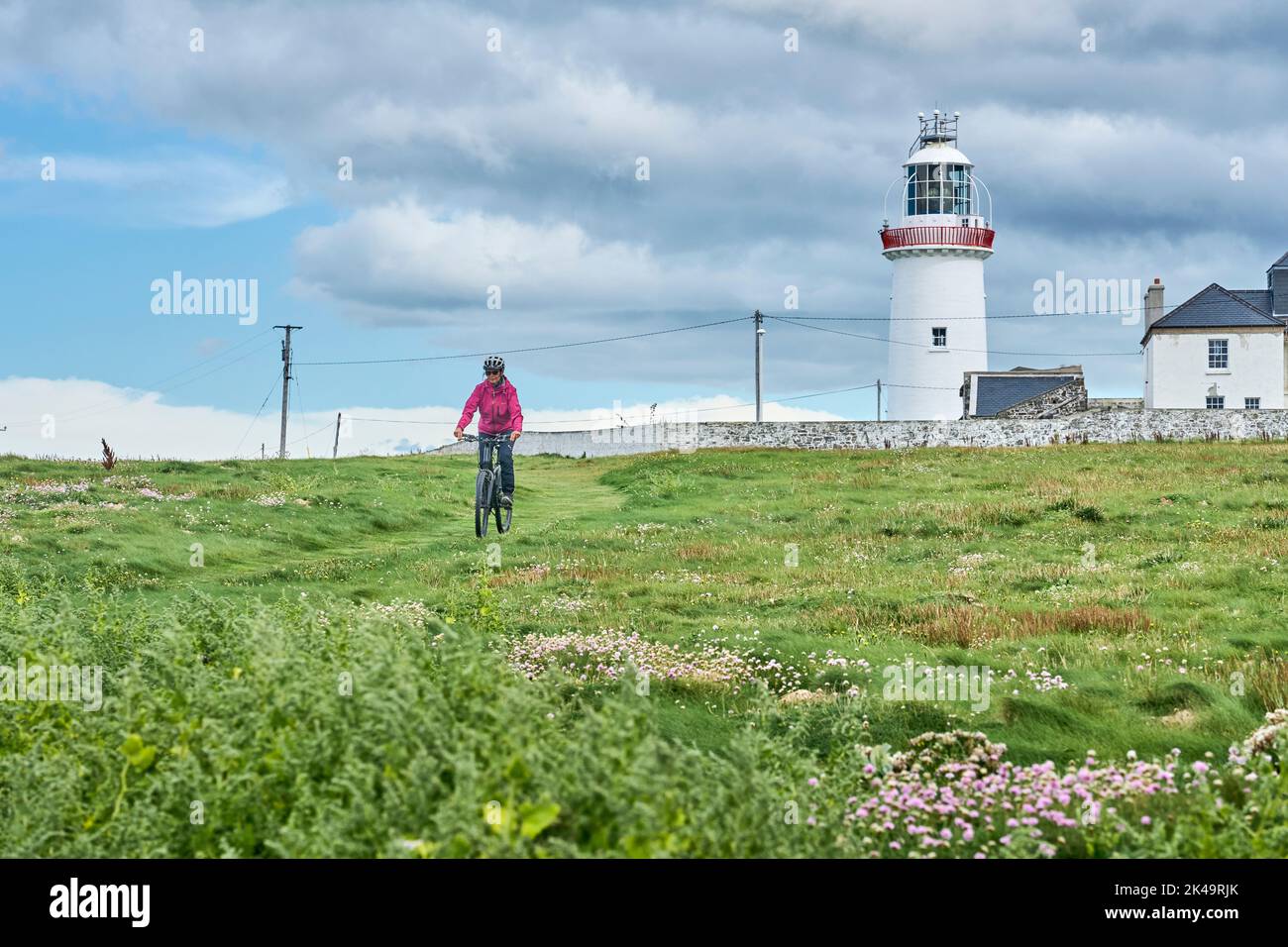 Mujer joven de Niza en bicicleta de montaña, en bicicleta en el faro de Dunmore Head cerca de Kilballyowen, condado de Limerick en el suroeste de Irlanda Foto de stock