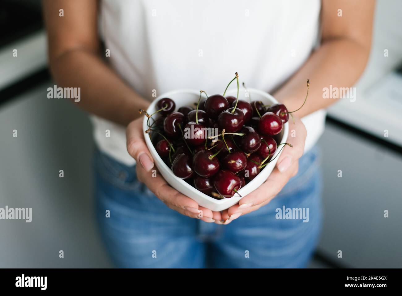 Cerezas maduras jugosas en un plato en las manos de las mujeres. Alimentos orgánicos saludables y naturales Foto de stock