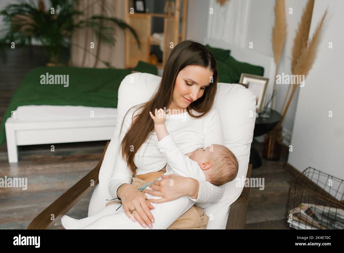 Mujer joven amamantando a su bebé en casa sentada en una silla Foto de stock