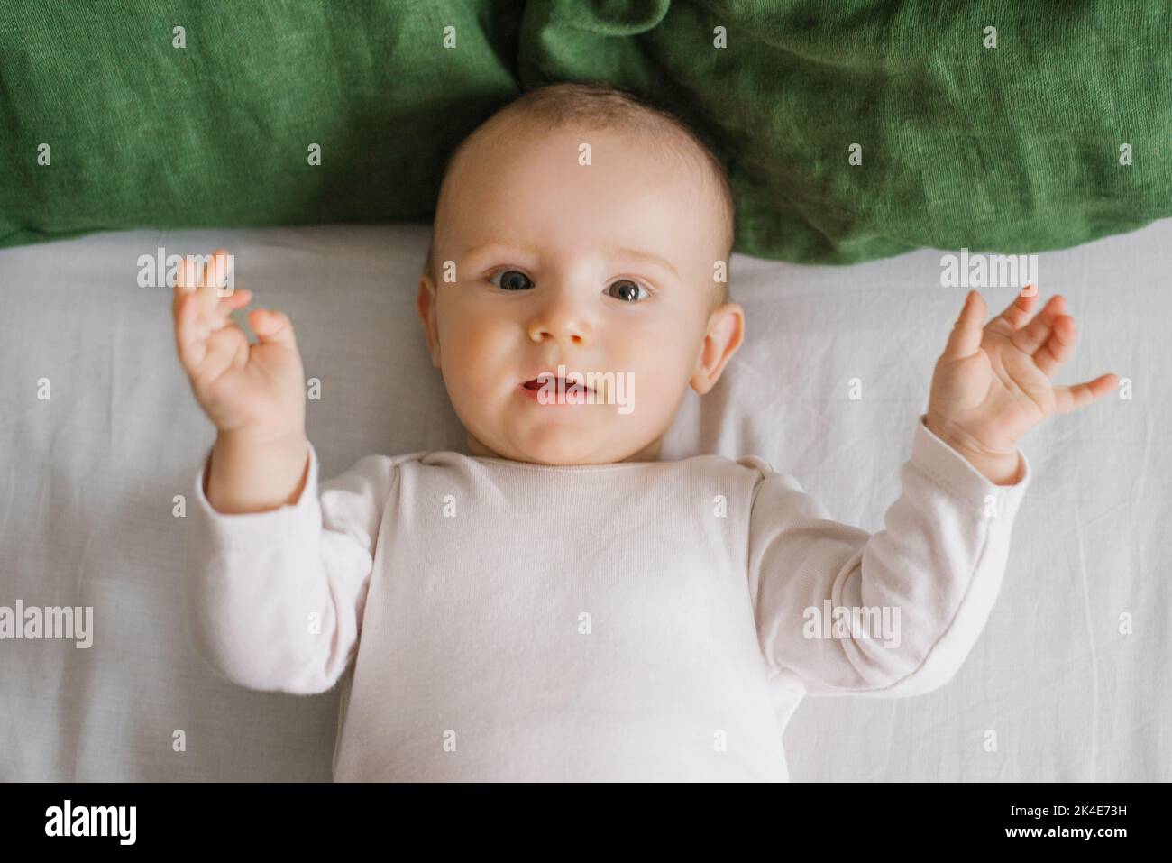 Retrato de un encantador y gracioso muchacho blanco caucásico de seis meses de edad, recostado en una cama y mirando a la cámara. Vista desde arriba. Un feliz Foto de stock