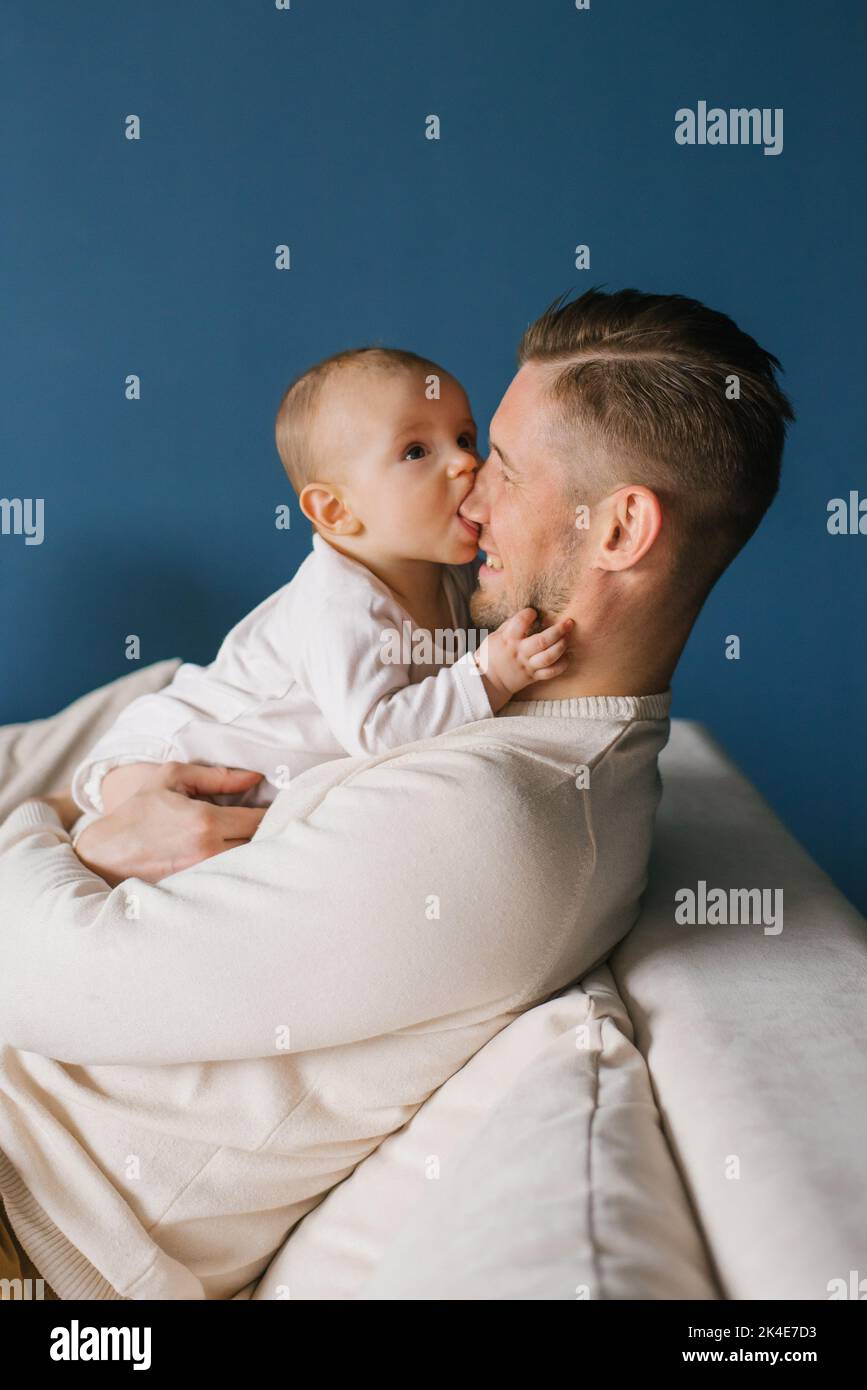 Un bebé de seis meses de edad en los brazos de su feliz padre, tratando de morderse la nariz. El niño está dentición Foto de stock