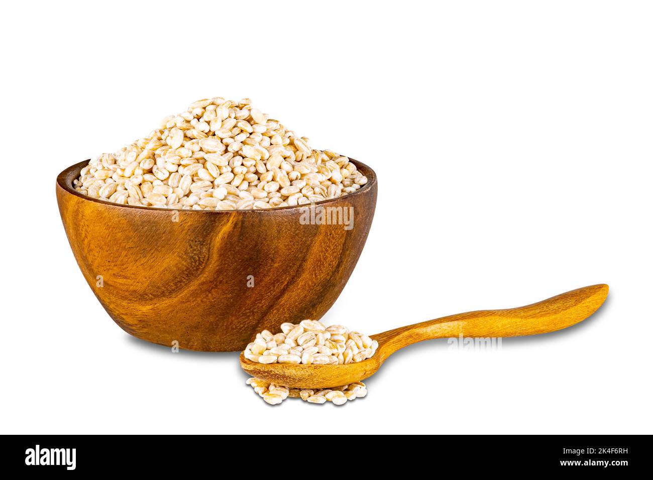 Vista de cebada perlada seca en un tazón de madera y una cuchara de madera sobre fondo blanco con camino de corte. Foto de stock