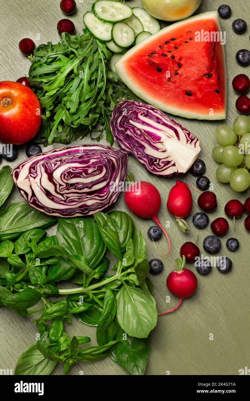 Juego de verduras de colores, frutas y bayas. Ramitas de albahaca verde y rúcula. Colocación plana. Fondo verde. Foto de stock