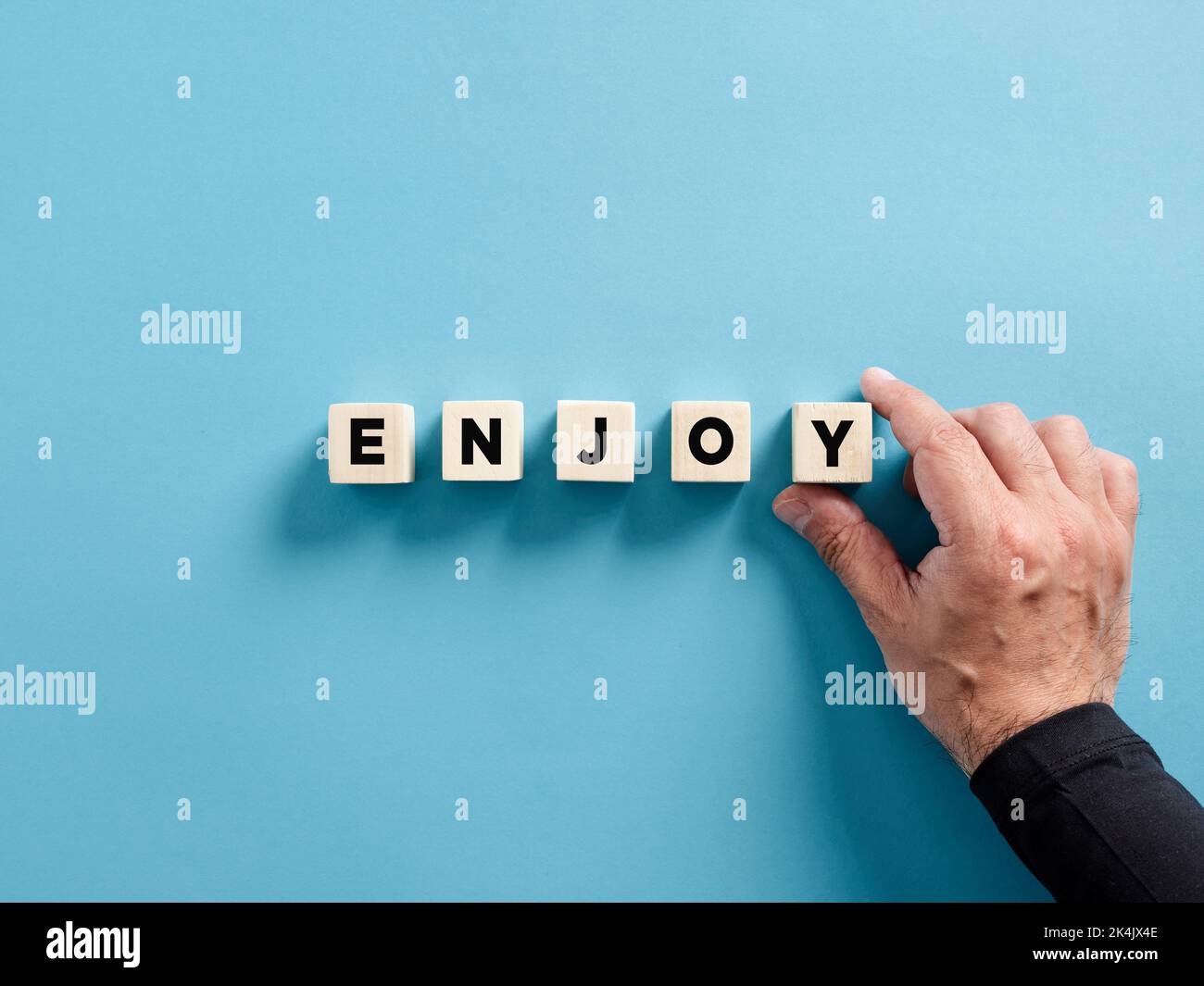 Mano masculina colocando los cubos de madera con la palabra disfrutar. Concepto de pensamiento positivo. Foto de stock