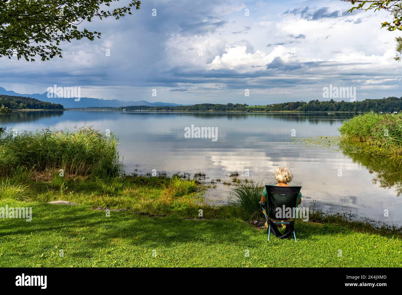 Eine Frau sitzt am Ufer des Simssee bei Bad Endorf, Bayern, Deutschland | lWoman sentada en el lago de Simssee cerca de Bad Endorf, Baviera, Alemania Foto de stock
