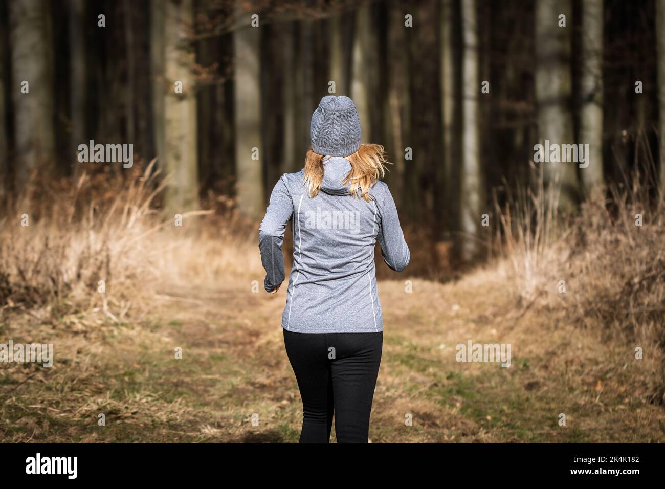 Mujer con gorro de punto corriendo al aire libre. Gimnasio, jogging en el bosque de otoño. Entrenamiento deportivo y estilo de vida activo en otoño Foto de stock