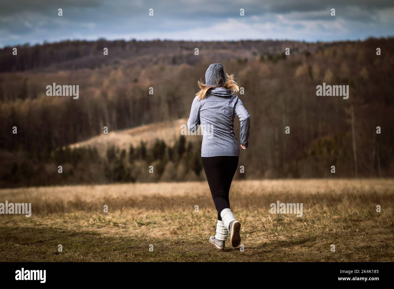 Mujer corriendo en la naturaleza del otoño. Actividad de fitness al aire libre. Atleta con gorro de punto, sudadera con capucha, leggings y calentadores de piernas durante los entrenamientos deportivos Foto de stock