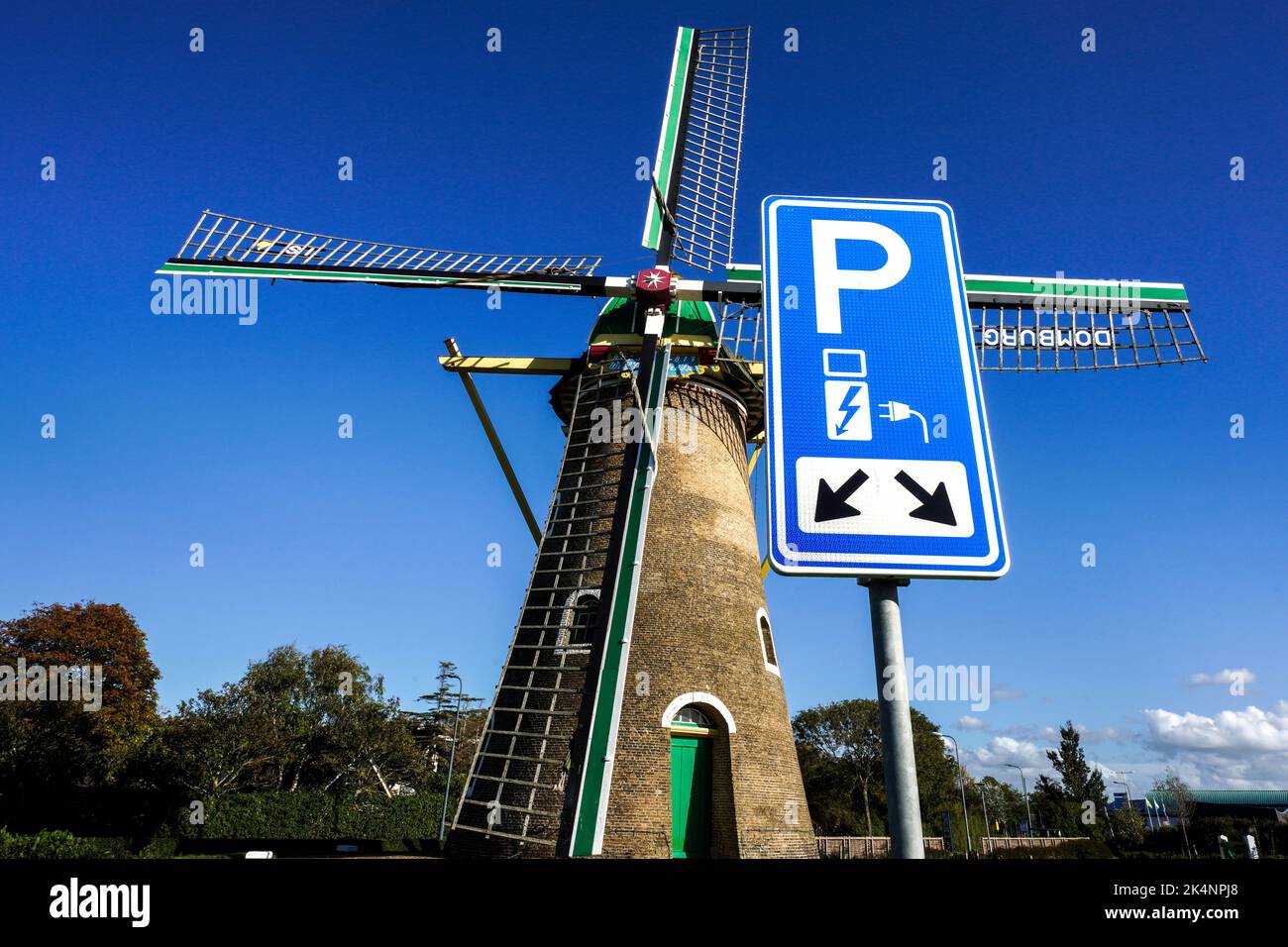 Electricidad a partir de la energía eólica: Aparcamiento con punto de carga para vehículos eléctricos frente al histórico molino de viento de 1817 en Domburg, Países Bajos Foto de stock