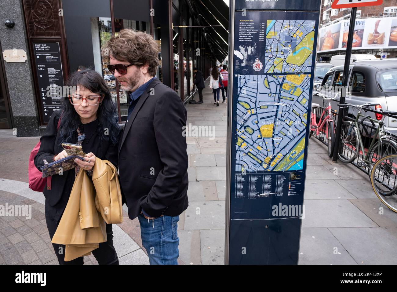 Dos personas mirando un smartphone para encontrar direcciones junto a un mapa de la zona de Knightsbridge el 7th de septiembre de 2022 en Londres, Reino Unido. Foto de stock