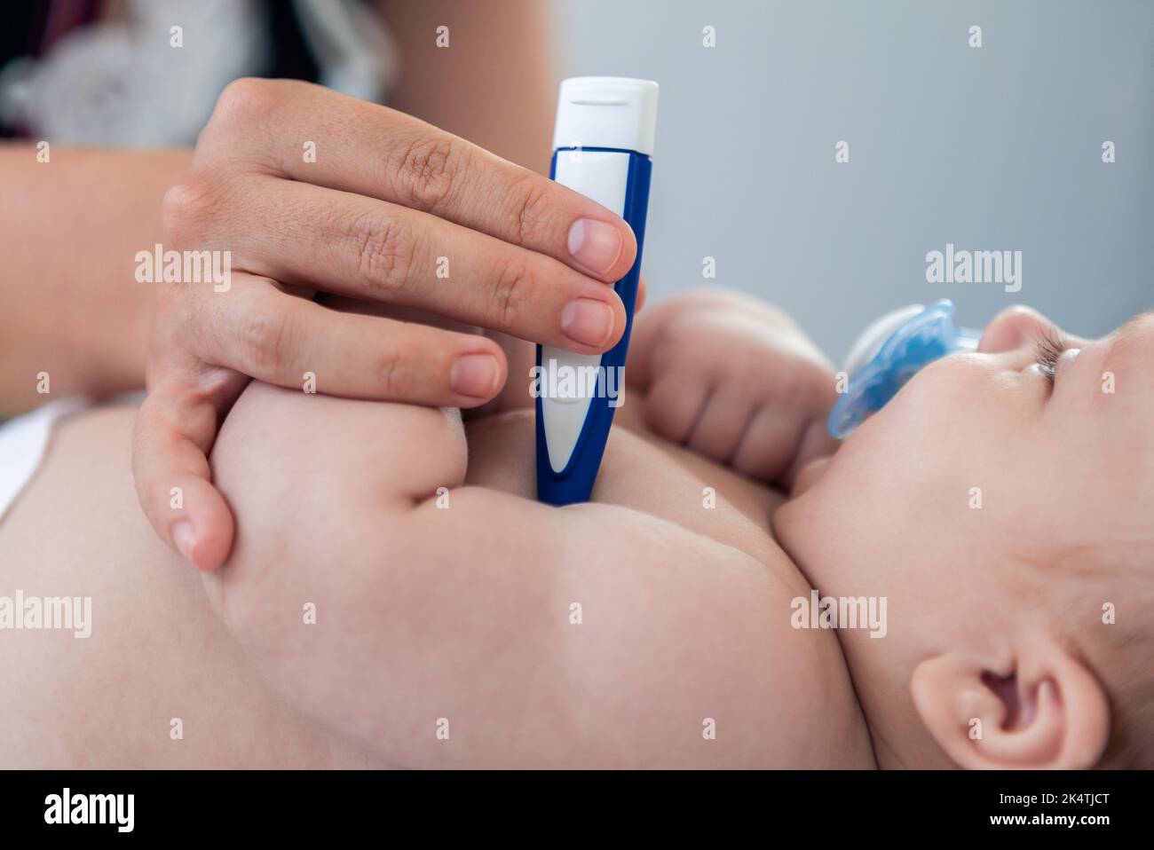 Médico mujer que examina al bebé niño pequeño con un termómetro para la fiebre de la gripe. Una enfermera que se somete a un chequeo médico con un pequeño paciente recién nacido enfermo en la clínica. Foto de stock