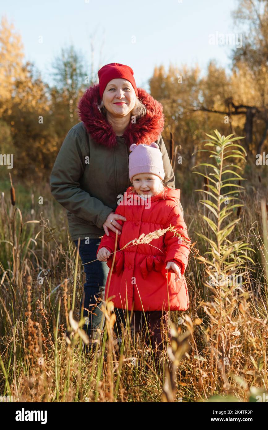 Una niña con un abrigo rojo camina por la naturaleza en un bosque de otoño  con su abuela. La época del año es el otoño Fotografía de stock - Alamy
