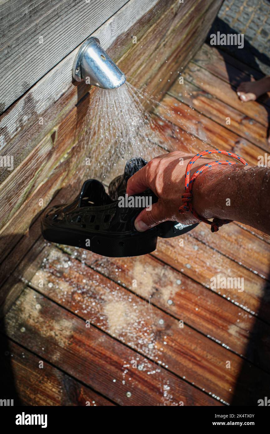 Sujetar las manos y enjuagar los zapatos de plástico para el agua bajo la ducha de playa Foto de stock