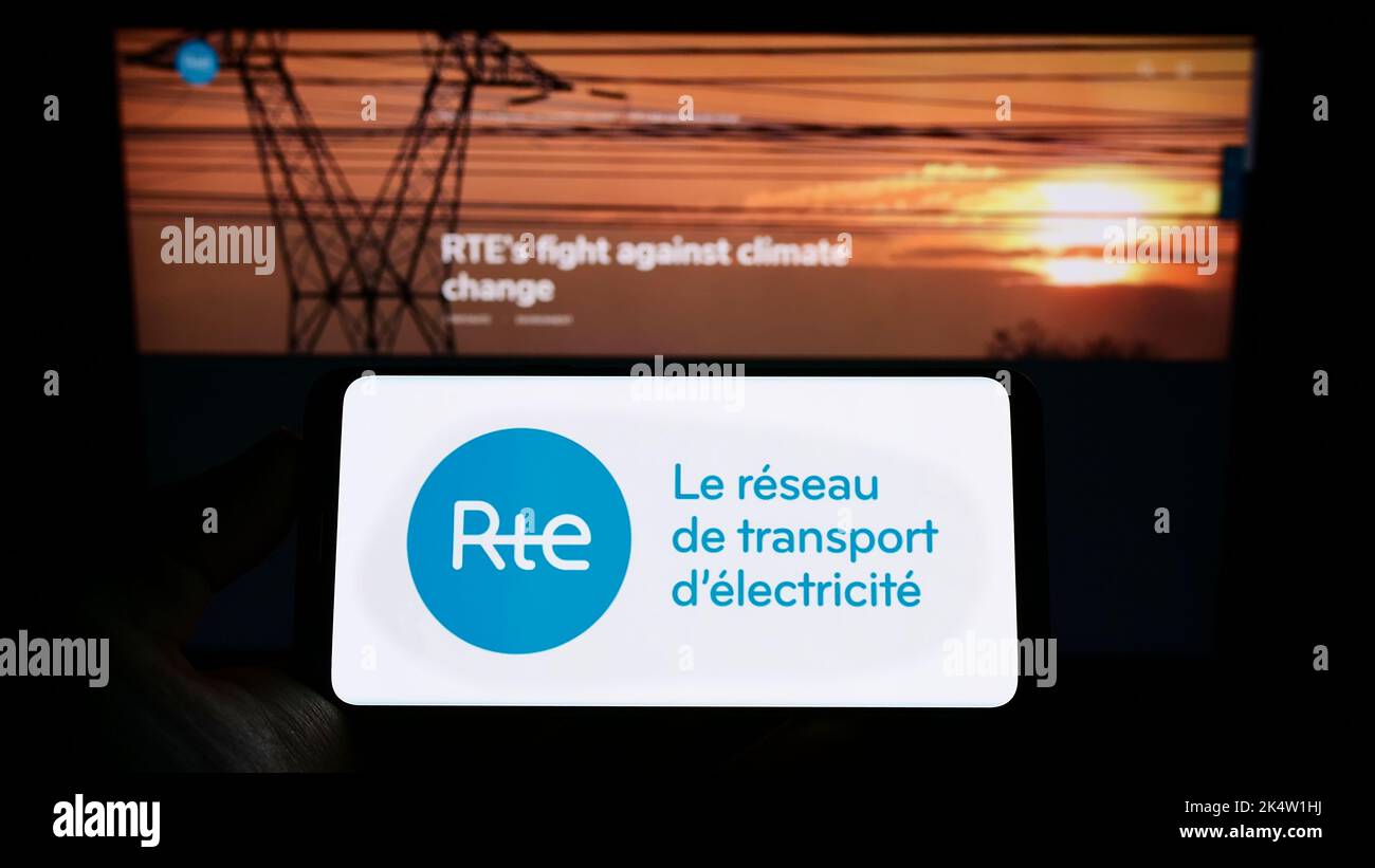 Persona que sostiene el celular con el logo de Reseau de Transport d'Electricite S.A. (RTE) en la pantalla delante de la página web del negocio. Enfoque la pantalla del teléfono. Foto de stock