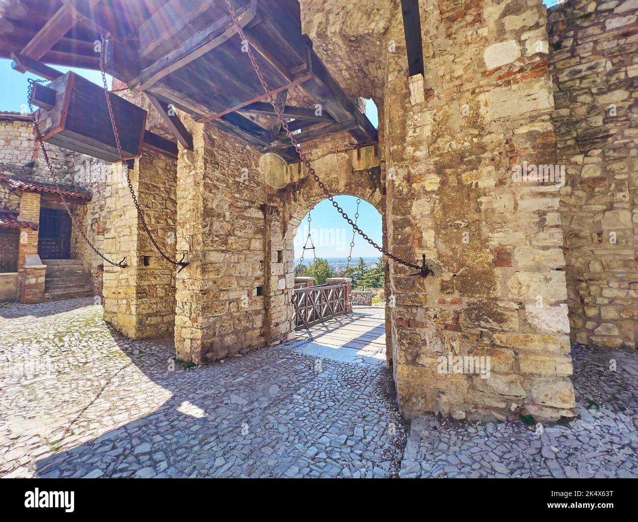 Histórico castillo de Brescia con cancha de piedra, enorme puerta con detalles de madera y puente de madera detrás del arco de paso, Italia Foto de stock